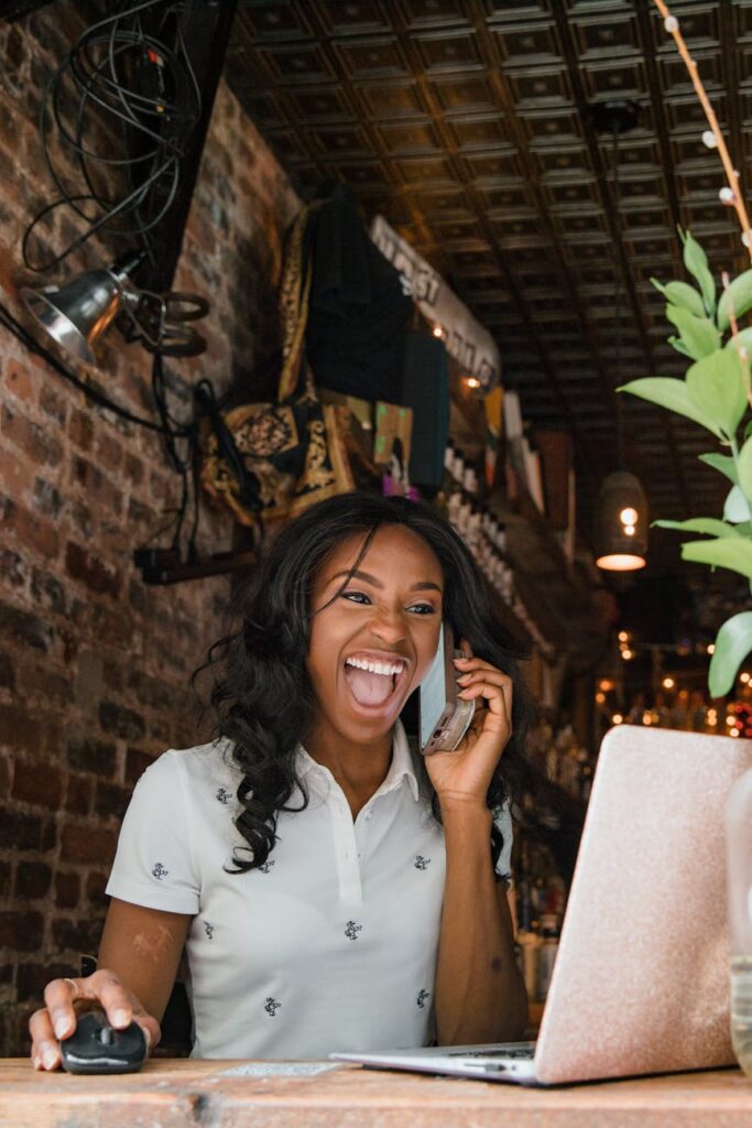 woman working on laptop on window sill and talking on phone